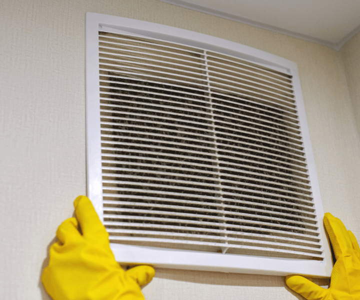 A professional cleaner wiping down a bathroom vent cover in Austin, TX.